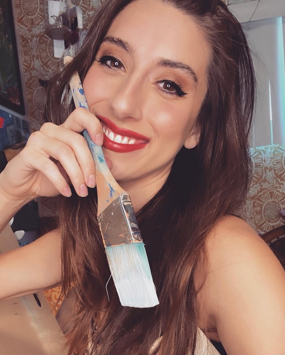 Taylor Christine smiling, holding a paintbrush to her cheek